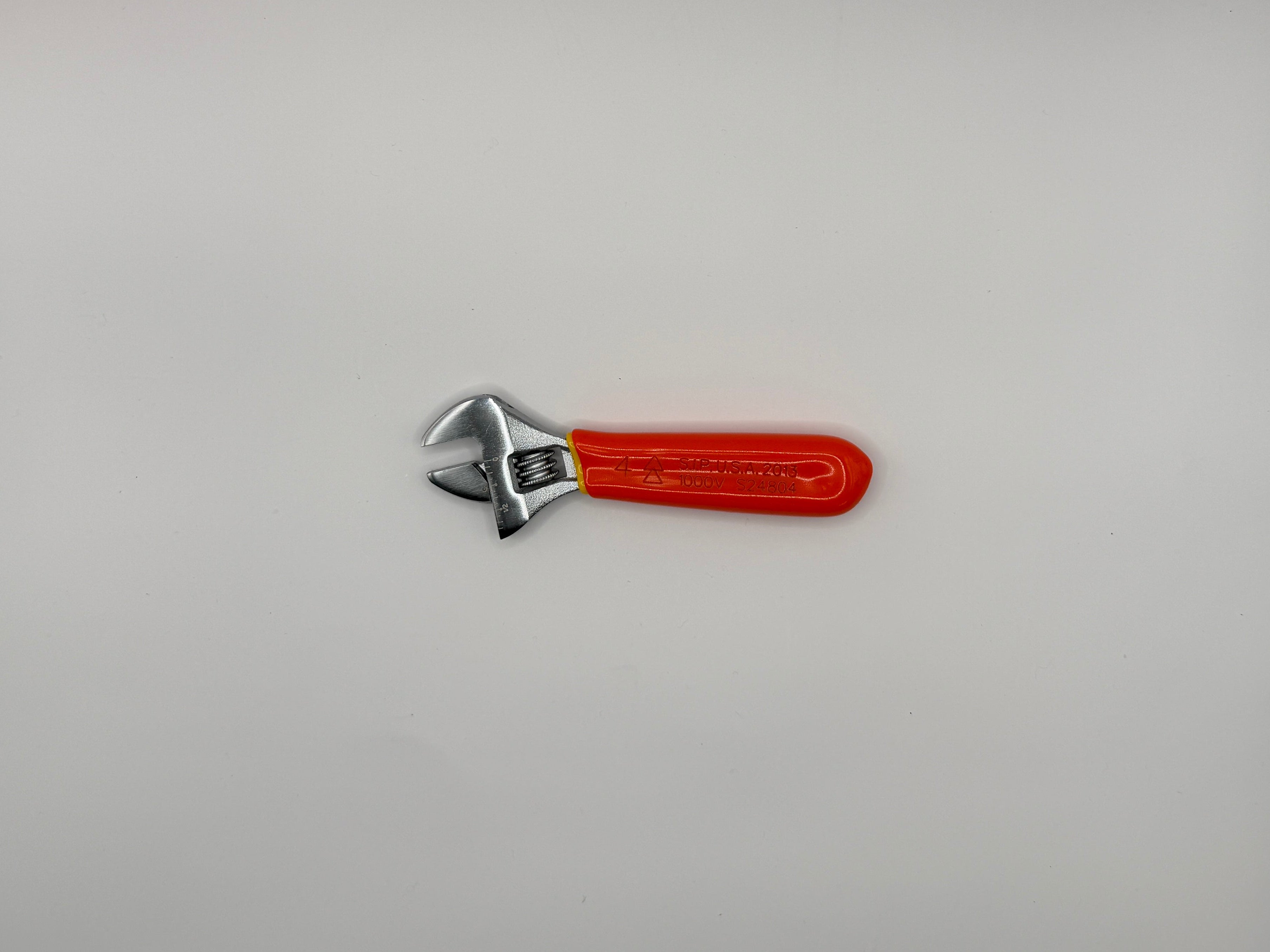 A small adjustable wrench with a bright red handle and silver metal head, photographed inside a white box corner.
